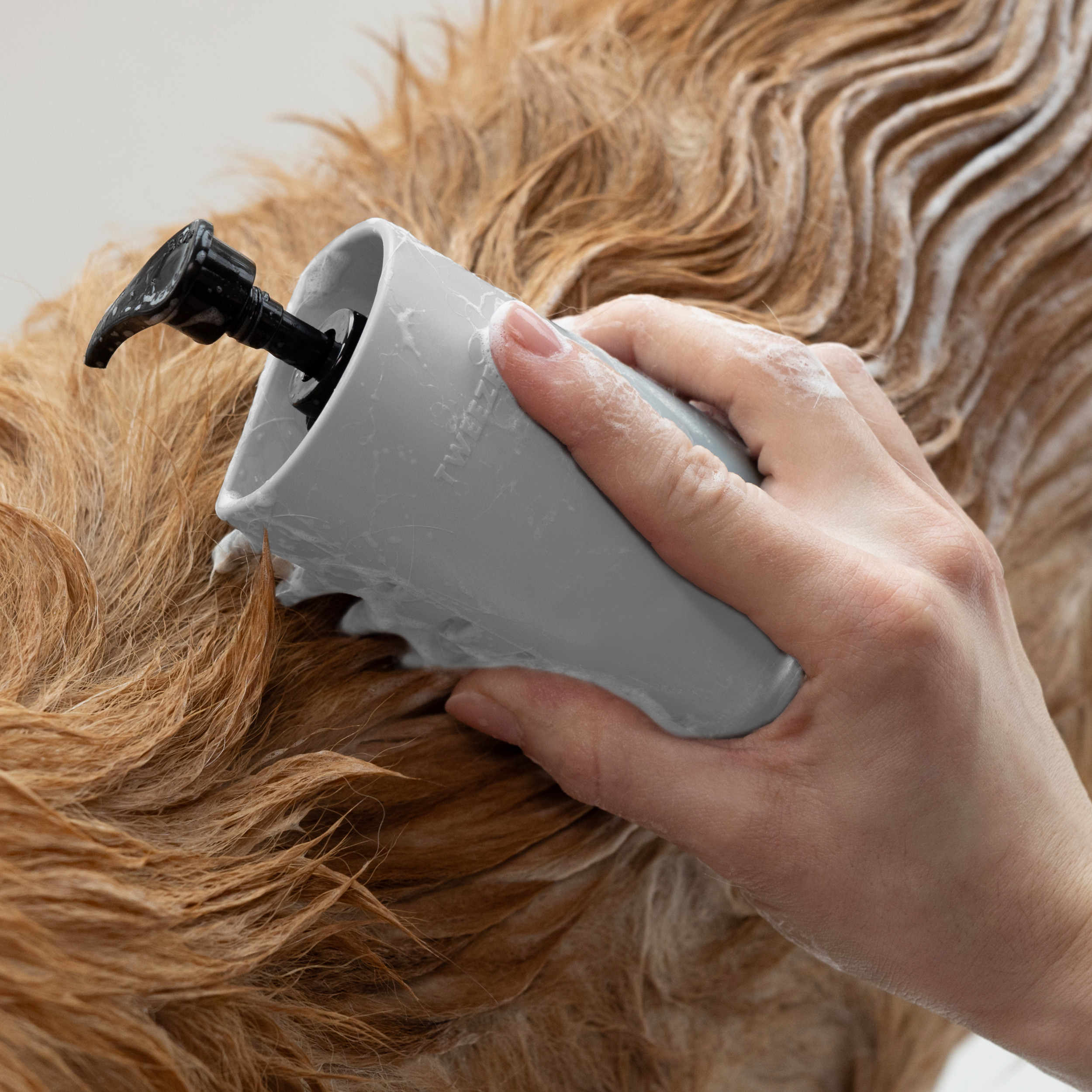 Hand holding 2-In-1 Shampoo Dispensing Bath Brush with bristles brushing dog's coat