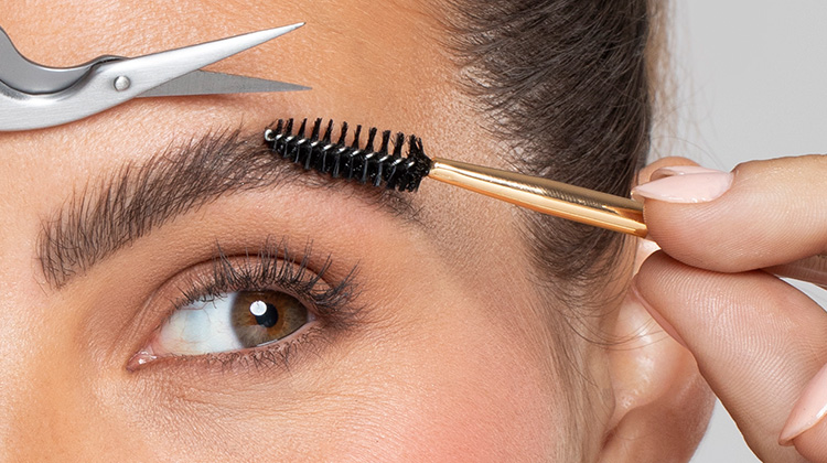 model with brow scissors and brush, brush is pushing eyebrow hairs upwards and scissor is above brow